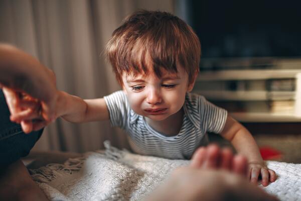 Crying child at a table with parent reaching out to hold his hand.