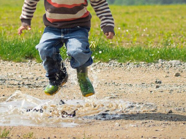 Little boy jumping in a mud puddle near a field.