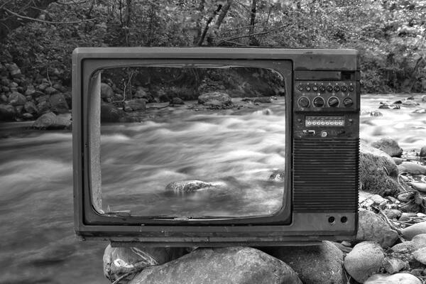 TV set with a hollow back on a rock by a river so you can see the river through the TV.
