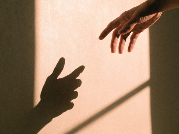 Image of a hand reaching out over a wall toward the shadow cast by the same hand.